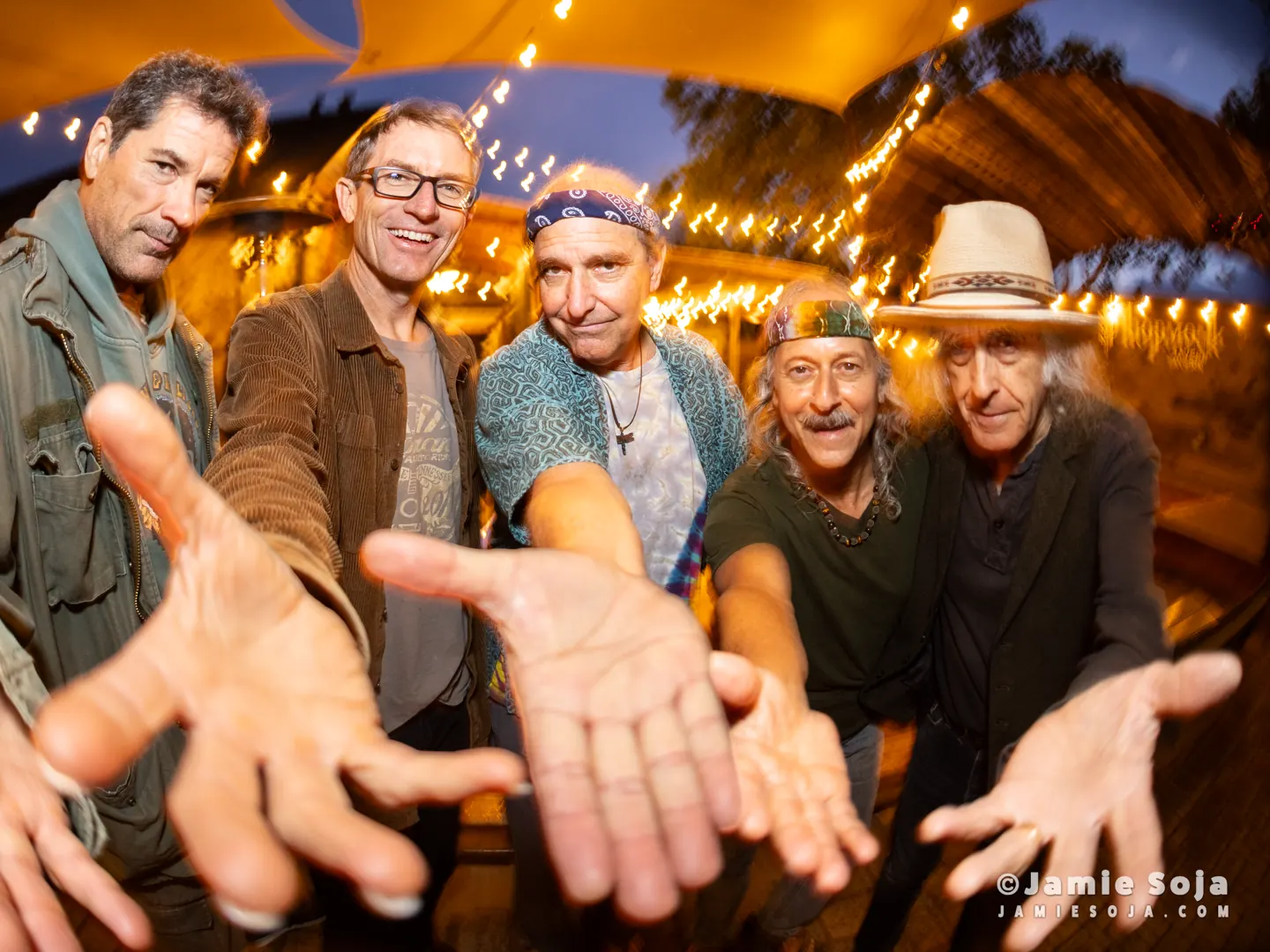 The five members of Skeleton Crewe reaching toward the camera under string lights